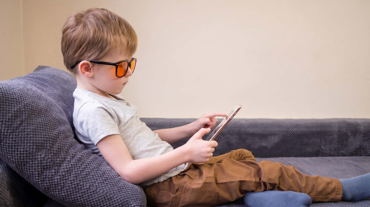 Niño con gafas de luz azul sin graduar usando una tablet
