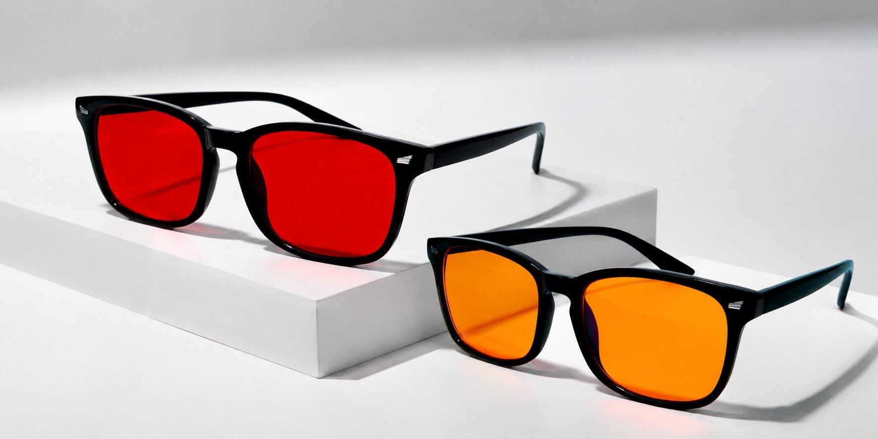 Gafas de luz azul Orenza con lente naranja y lente roja sobre fondo neutro